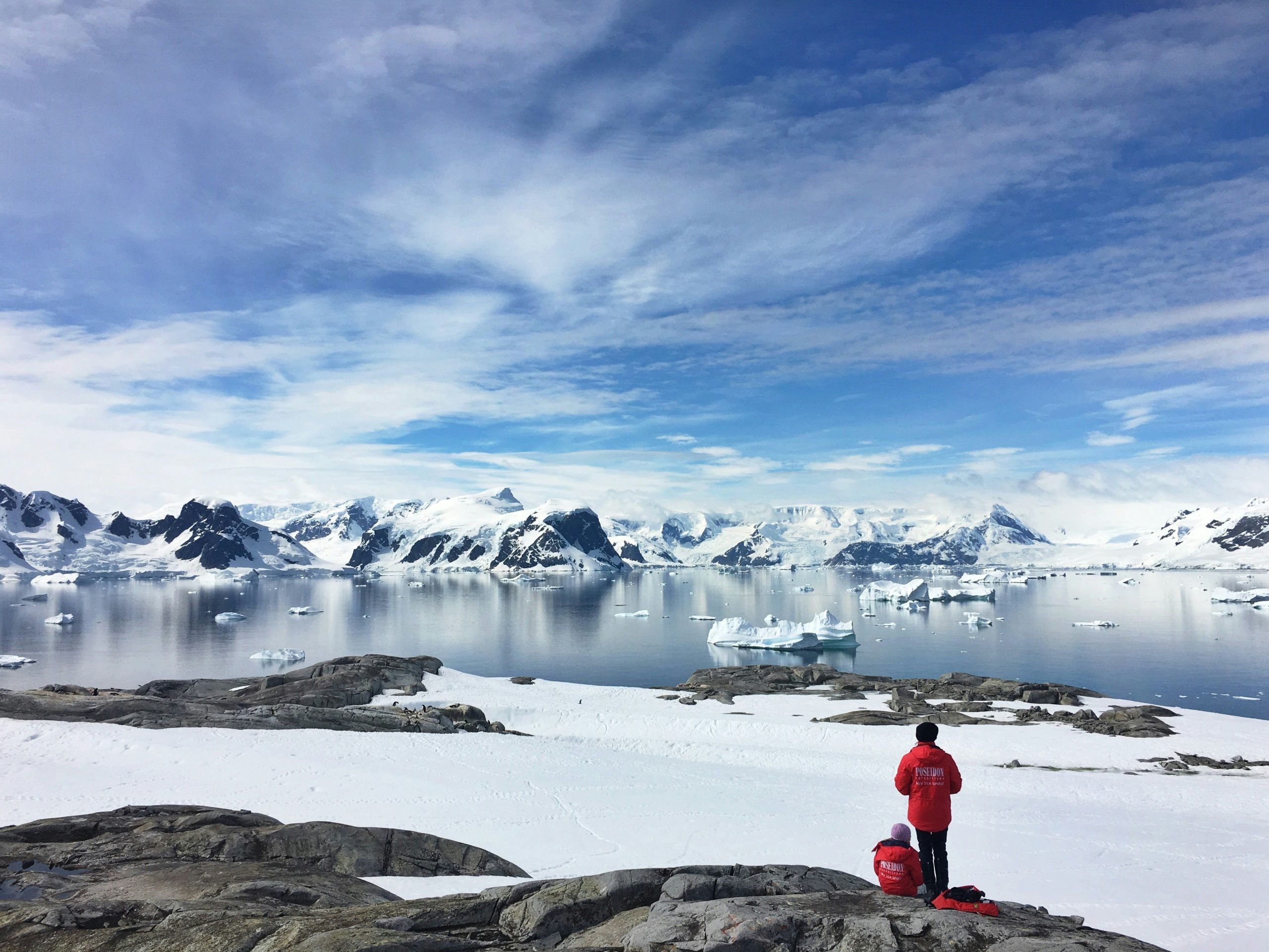 Travelers taking in panoramic views of glassy waters and snow-capped peaks in Antarctica